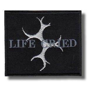 Pode incluir: Patch quadrado preto com as palavras "LIFE CRIED" em cinza, com um design de árvore cinza estilizado. O patch tem uma borda preta e é provavelmente feito de tecido.