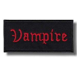 Puede incluir: Parche rectangular negro con la palabra "Vampire" bordada en rojo con letras góticas. El parche está hecho de una tela texturizada y tiene un diseño limpio y sencillo.