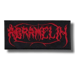 以下が含まれることがあります： 黒い長方形のパッチ。赤色のゴシック様式の文字で「ABRAMELIN」と刺繍されています。パッチには黒い縁取りがあり、衣服やアクセサリーに縫い付けるように設計されています。