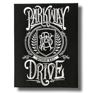 May include: A black rectangular patch with white, decorative lettering. The text reads "Parkway Drive" above and "Drive" below a central emblem. The emblem features a shield with intertwined letters and the text "Byron Bay".