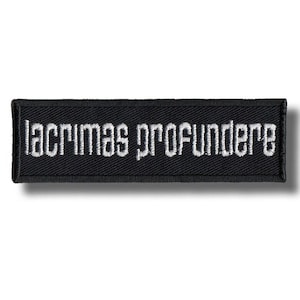 Peut inclure: Un écusson rectangulaire noir avec le texte brodé en blanc "lacrimas profundere". L'écusson a une bordure noire et est probablement conçu pour être cousu ou repassé sur des vêtements ou des accessoires.