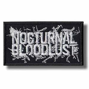 以下が含まれることがあります： 黒い長方形のパッチで、白の刺繍で「NOCTURNAL BLOODLUST」と書かれています。パッチには黒い縁取りと白い装飾的なデザインがあります。このパッチは、ジャケットやバッグ用です。
