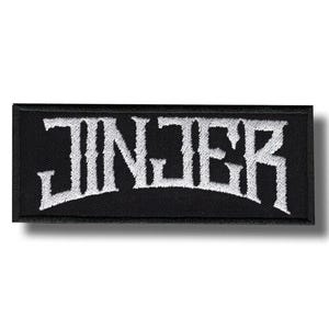 May include: Black rectangular patch with the word "JINJER" embroidered in white, stylized, gothic lettering. The patch has a black border and is likely designed to be sewn or ironed onto clothing or accessories.