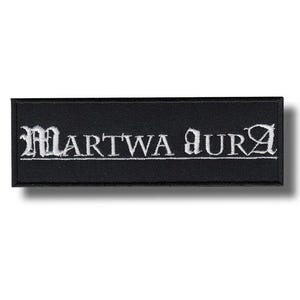 May include: Black rectangular patch with the embroidered text "MARTWA AURA" in white gothic lettering. The patch has a black border and is likely made of fabric.