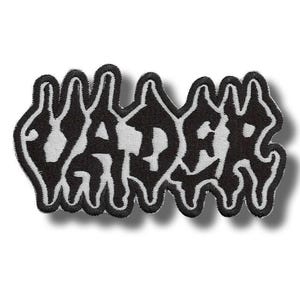 May include: A black and white embroidered patch with the word "VADER" in a stylized, dripping font. The patch has a white background and a black border, creating a bold contrast. The patch is rectangular in shape.
