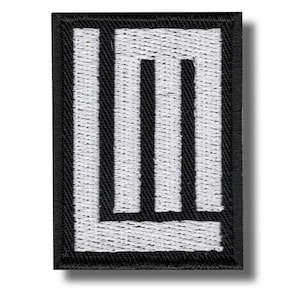 以下が含まれることがあります： 黒い縁取りと白い「LM」デザインが施された刺繍パッチ。文字は太くブロック状で、質感があります。パッチは長方形で、影があります。
