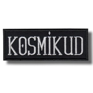 Puede incluir: Parche rectangular negro con la palabra "KOSMIKUD" bordada en blanco. El parche tiene un borde negro y un efecto de sombra. Este parche es probablemente para ropa o accesorios.