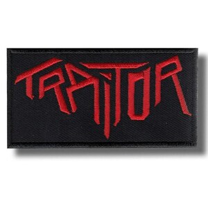 May include: A black rectangular patch featuring the word "TRAITOR" in bold, red, embroidered lettering. The patch has a black border. The design is likely intended for application to clothing or accessories.