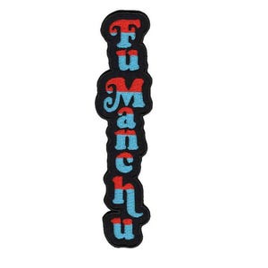 May include: Embroidered patch featuring the text "Tu Manchu" in a vertical layout. The letters are in red and blue, with a retro font style. The patch is outlined with a black border.