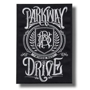 May include: Black rectangular patch with white embroidered text and design. The text reads "PARKWAY DRIVE" above a shield with the initials "P D A" and "BYRON BAY" below. The design includes a laurel wreath and decorative flourishes.