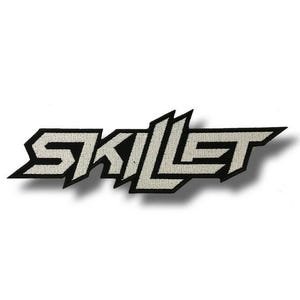 Può includere: Una toppa ricamata in bianco e nero con la scritta "SKILLET" in un carattere stilizzato e angolare. Le lettere sono grigio chiaro con un bordo nero, creando un design audace. La toppa è destinata all'abbigliamento o agli accessori.