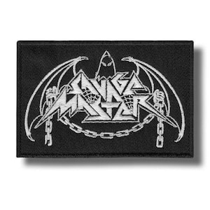 Peut inclure: Écusson rectangulaire noir avec texte et graphiques brodés en blanc. Le texte se lit "SAVAGE MASTER" dans une police stylisée, avec une figure ailée de chauve-souris au-dessus et des chaînes en dessous. L'écusson est probablement destiné à un groupe ou à des produits dérivés.