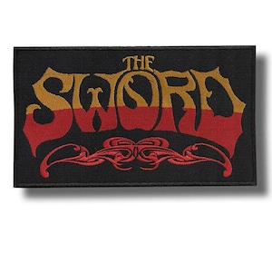 May include: Black rectangular patch with the words "THE SWORD" in gold and red, with an ornate red design at the bottom. The patch is likely for a jacket or bag, and features a vintage, rock-and-roll aesthetic.