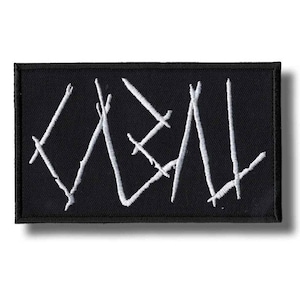Puede incluir: Parche rectangular negro con la palabra "KVEN" bordada en blanco. Las letras están estilizadas con líneas angulares y barras transversales. El parche tiene un borde negro y es probablemente un accesorio para ropa o bolsos.