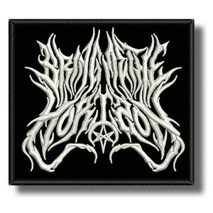 Puede incluir: Parche bordado con el texto blanco "BEHEMOTH" en una fuente gótica estilizada, con un símbolo de pentagrama, sobre un fondo cuadrado negro. El parche tiene un borde negro.