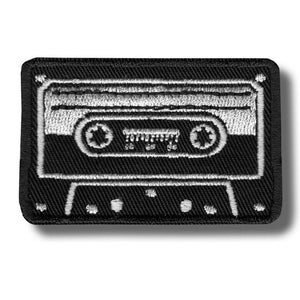 Op de afbeelding: Zwart en wit geborduurde patch met een cassettebandje ontwerp. De patch heeft een rechthoekige vorm met afgeronde hoeken en een zwarte rand. Het cassettebandje ontwerp is gedetailleerd met witte stiksels.