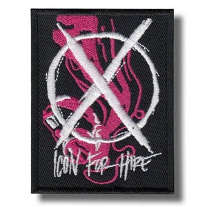 May include: Black rectangular patch featuring a white embroidered circle with a white X crossing it. A pink design is visible within the circle. The words "ICON FOR HIRE" are embroidered in white below.