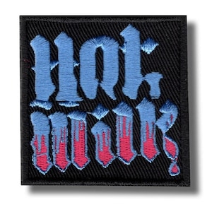 Op de afbeelding: Geborduurde patch met de woorden "Hot Milk" in een gotisch lettertype. De tekst is lichtblauw met rode druipaccenten, op een zwarte vierkante achtergrond.