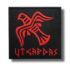 May include: A black square patch featuring a red embroidered bird design and the word "UTGARDAS" in red. The bird is stylized with detailed patterns, and the text is in a distinctive font. The patch is suitable for clothing or accessories.