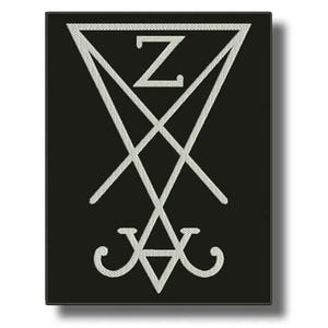 May include: Black rectangular patch with a white, stylized symbol. The symbol includes a triangle at the top, an intersecting X shape, and a triangle at the bottom. The letter "Z" is inside the top triangle. The patch has a black border.