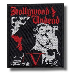 以下が含まれることがあります： 黒色の刺繍パッチ。赤色のゴシック体で「Trollywood Undead」の文字が書かれています。パッチには、子供のグレースケールイラストと赤い「V」が描かれています。