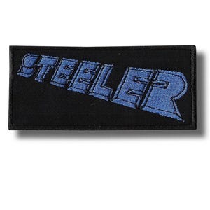 May include: A black rectangular patch featuring the word "STEELER" in blue, with a shadow effect. The patch has a black border and is designed to be sewn or ironed onto clothing or fabric.