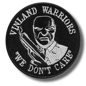 May include: A round black and white embroidered patch featuring a stern-faced man holding a gun. The text "VINLAND WARRIORS" arcs around the top, with "WE DON'T CARE" at the bottom. The design is detailed and bold.