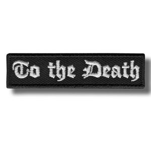 Può includere: Toppa rettangolare nera ricamata con la scritta "To the Death" in lettere gotiche bianche. La toppa ha un bordo nero ed è progettata per essere cucita su abiti o accessori.