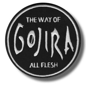 May include: A black, circular patch with white embroidered text. The text reads "THE WAY OF GOJIRA" in a stylized font, with "ALL FLESH" below. The patch has a white border and is likely for clothing or accessories.
