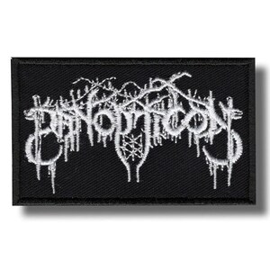 Può includere: Toppa rettangolare nera con testo ricamato bianco. Il testo stilizzato sembra essere un logo di una band. Il design include dettagli intricati e un effetto gocciolante, creando un'estetica gotica o metal.