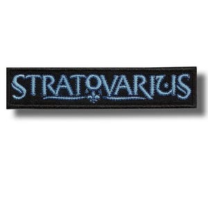 Può includere: Toppa rettangolare nera con la scritta "STRATOVARIUS" ricamata in blu chiaro, con un carattere stilizzato. Un piccolo motivo floreale è centrato sotto il testo. Ideale per abbigliamento o accessori.