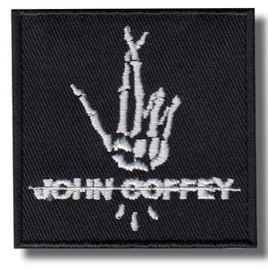 May include: Black square patch featuring a white embroidered skeleton hand gesture. The text "JOHN COFFEY" is embroidered below the hand, with a line through the name.