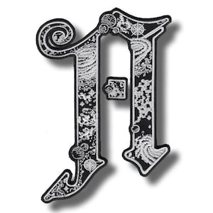 Op de afbeelding: Zwart en wit geborduurde patch in de vorm van de letter "A". De patch heeft ingewikkelde hemelse en wervelende ontwerpen. De rand is zwart en de details zijn wit.