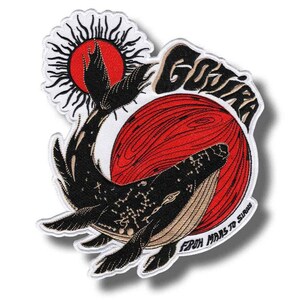 Pode incluir: Patch bordado com um design de baleia preta, um sol vermelho e a palavra "GOJIRA" em branco. O patch também inclui o texto "FROM MARS TO SURIS". O patch tem uma borda branca.