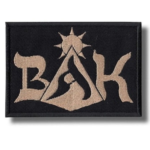 Peut inclure: Écusson rectangulaire noir avec les lettres "BAK" dans une police stylisée, avec un soleil et un motif de montagne au centre. Les lettres et le motif sont de couleur beige, et l'écusson a une bordure noire.