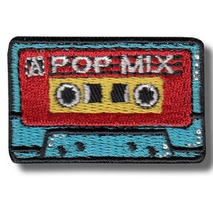 Può includere: Toppa ricamata con un design a cassetta retrò. La toppa ha una sezione superiore rossa con la scritta "POP MIX" in bianco, un centro giallo e un bordo azzurro. Il design ricorda la cultura musicale degli anni '80.