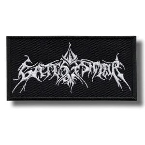 May include: Black rectangular patch with white stylized text. The text appears to be a band logo or emblem, featuring sharp, angular lines and a gothic aesthetic. The patch is likely made of fabric and designed to be sewn or ironed onto clothing or accessories.
