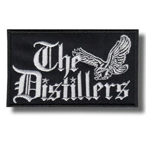 May include: Black rectangular patch featuring white embroidered text and a bird graphic. The text reads "The Distillers" in a gothic font. The bird is shown with outstretched wings.
