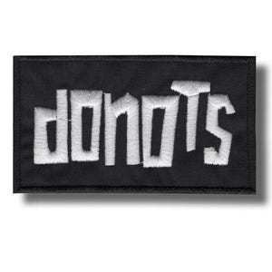 May include: A black rectangular patch featuring the word "DONOTS" embroidered in white. The letters are in a bold, stylized font. The patch has a black border and a shadow effect.