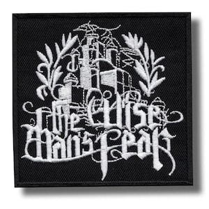 May include: Black square patch featuring white embroidered text and a design. The text reads "The Elise Mans Fear" in a gothic font, with a castle and floral design above. The patch has a black border.