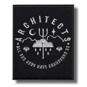 以下が含まれることがあります： 白の刺繍文字とグラフィックが入った黒色の長方形パッチ。「ARCHITECTS」の文字がアーチ状に、「ALL OUR GODS HAVE ABANDONED US」の文字が円形に配置されています。グラフィックには三叉の槍、雲、星が含まれています。