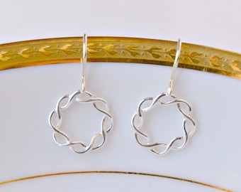 Könnte beinhalten: Ein Paar silberne Ohrringe mit einem runden, geflochtenen Design. Die Ohrringe hängen an einem weißen Teller mit goldfarbenem Rand.