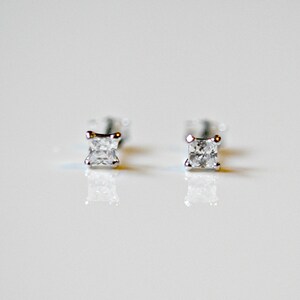 K&ouml;nnte beinhalten: Ein Paar quadratisch geschliffene Diamant-Ohrstecker. Die Diamanten sind in einer Fassung aus Silber oder Wei&szlig;gold gefasst. Die Ohrringe werden auf einer wei&szlig;en Oberfl&auml;che pr&auml;sentiert, die das Licht reflektiert.