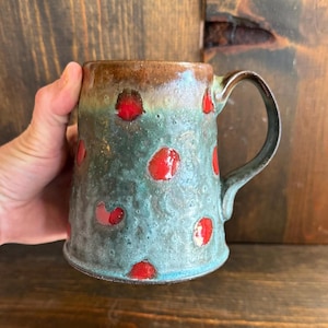 Puede incluir: Taza de cerámica hecha a mano con un esmalte turquesa texturizado y lunares rojos. El borde superior es de color marrón oscuro y el asa es de color gris oscuro. Una pieza única, hecha a mano para disfrutar del café o té.
