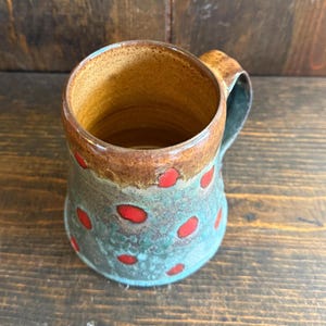 Puede incluir: Taza de cerámica hecha a mano con base turquesa, borde marrón y lunares rojos. El interior es de un cálido marrón dorado. El asa es de color turquesa a juego. Taza de café rústica única.