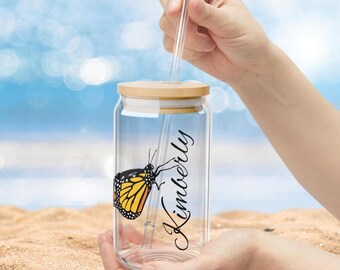 May include: A clear glass reusable water bottle with a bamboo lid and a straw. The bottle has a butterfly graphic and the name "Kimberly" printed on the side.
