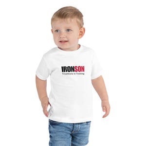 May include: White toddler t-shirt with black text that reads "IRONSON Triathlete in Training".