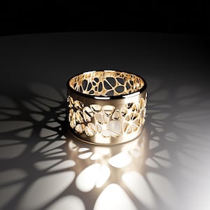 Peut inclure: Une bague en or avec un design délicat et complexe. La bague est faite d'un métal fin et a une bande large. Le design est un motif répétitif de petits cercles et ovales.