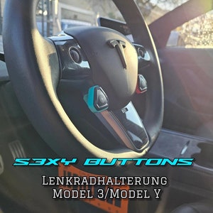 Peut inclure: Gros plan sur un volant en cuir noir avec un logo Tesla et des boutons bleus et orange. Le texte "S3XY BUTTONS LENKRADHALTERUNG MODEL 3/MODEL Y" est visible en bas de l'image.