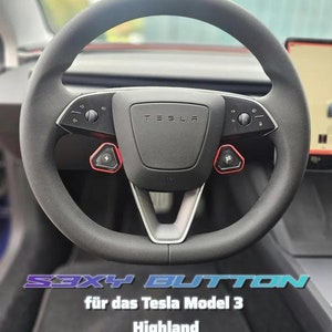 May include: A black leather steering wheel with a silver center and two red buttons labeled with lightning bolts. The steering wheel has a Tesla logo and the text "S3XY BUTTON" and "für das Tesla Model 3 Highland" on the bottom.
